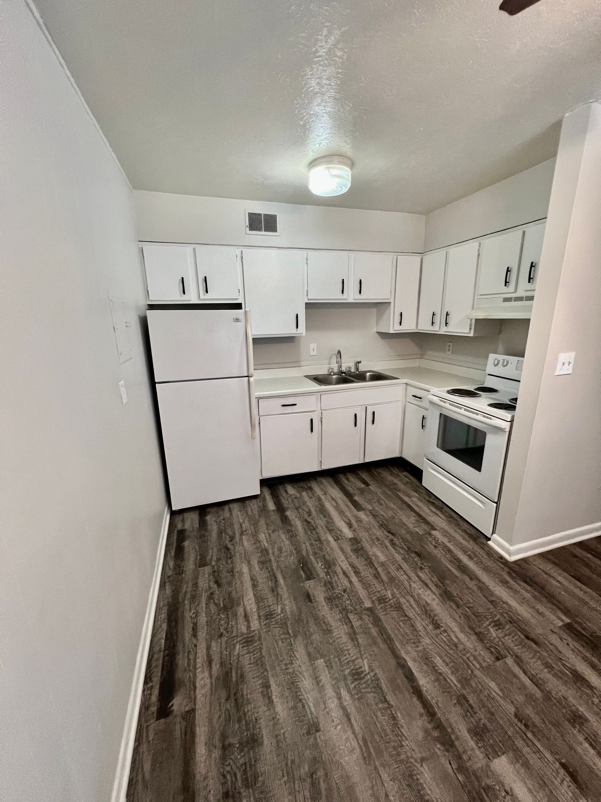 A kitchen with white cabinets , a refrigerator , a stove , and a sink.