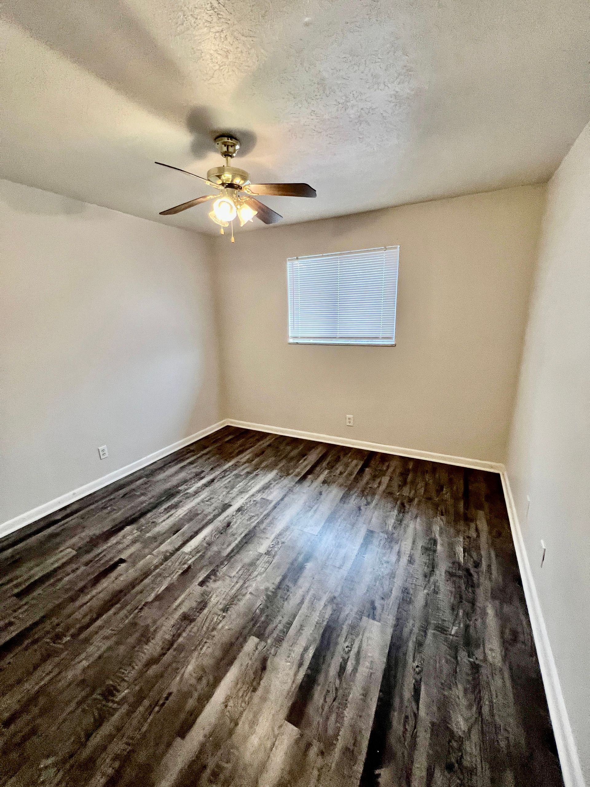 An empty bedroom with hardwood floors and a ceiling fan.
