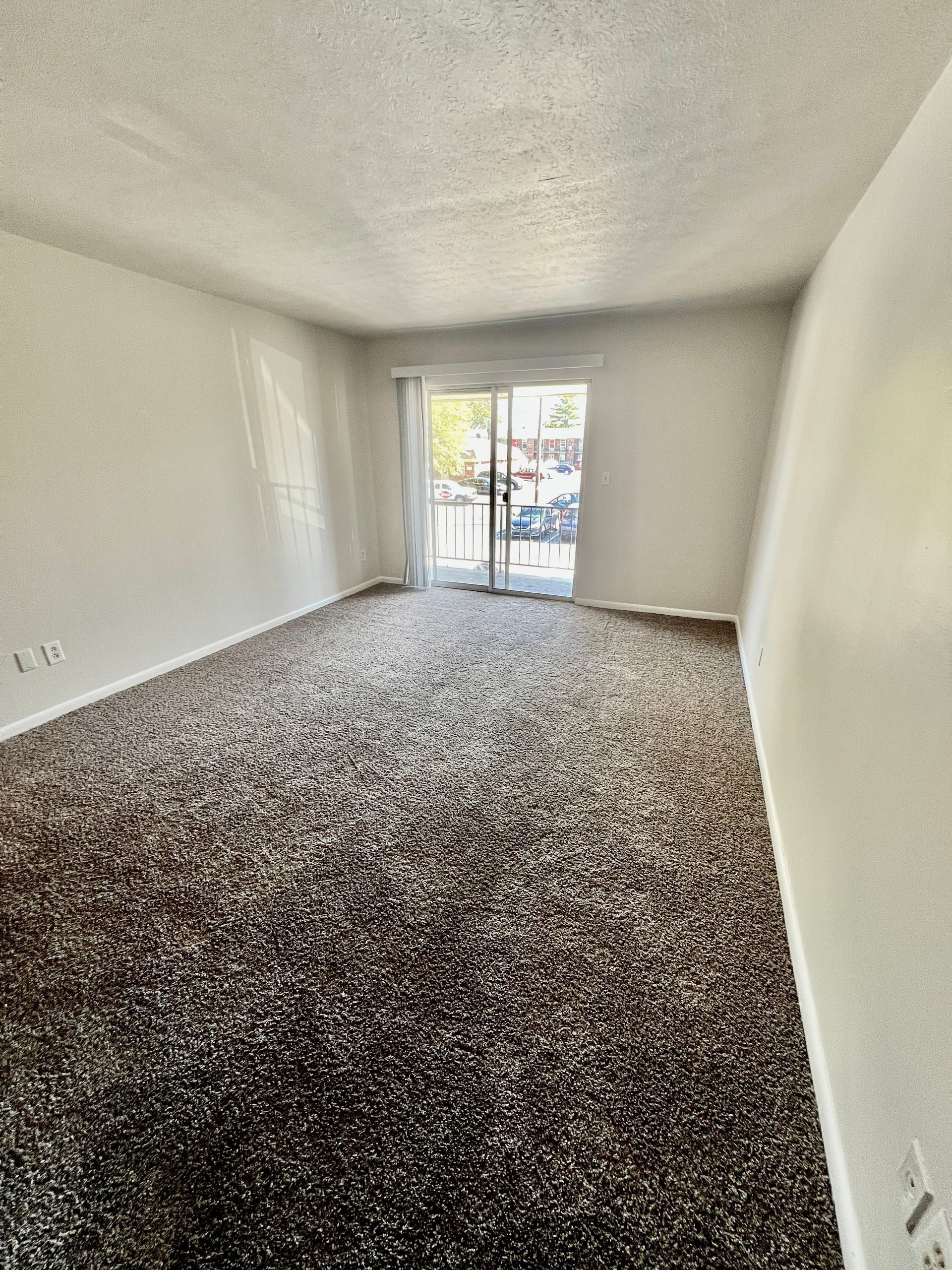 An empty living room with a sliding glass door and a carpeted floor.