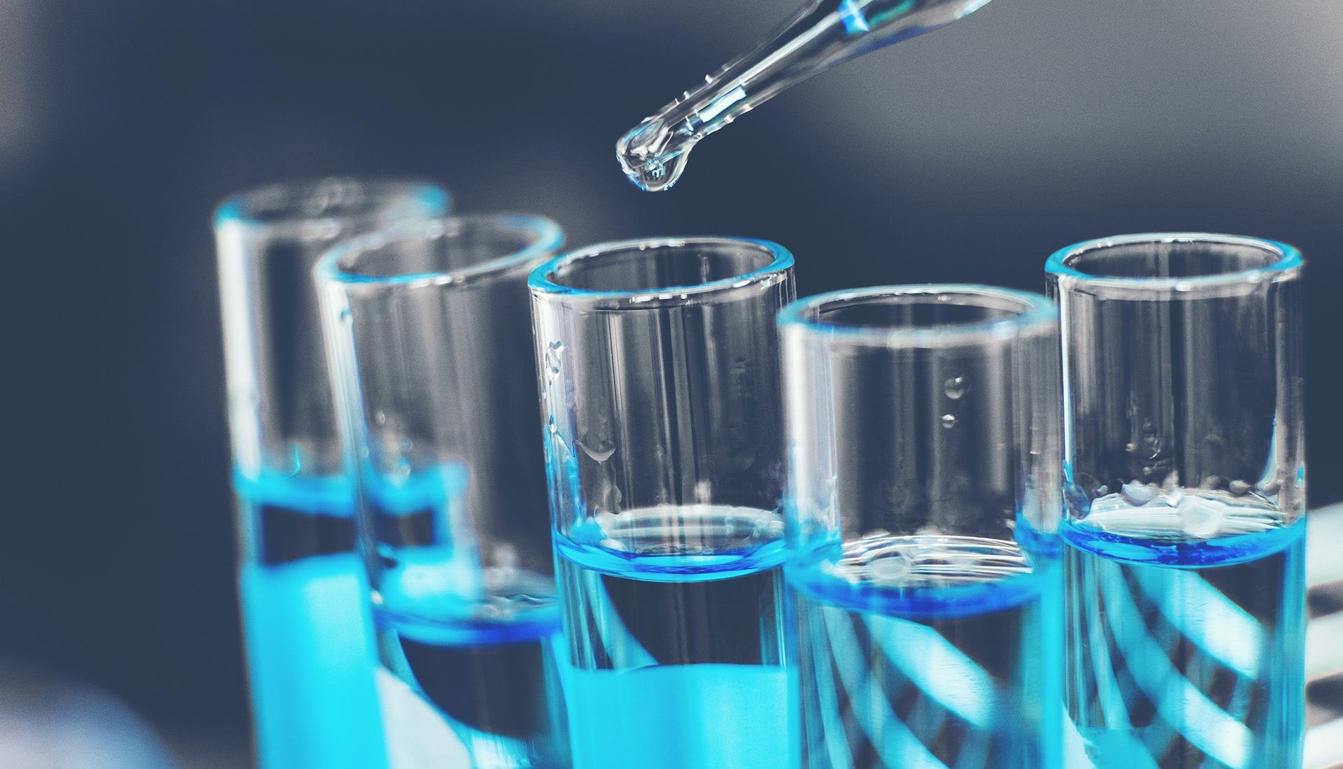A pipette is being poured into a row of test tubes filled with blue liquid.