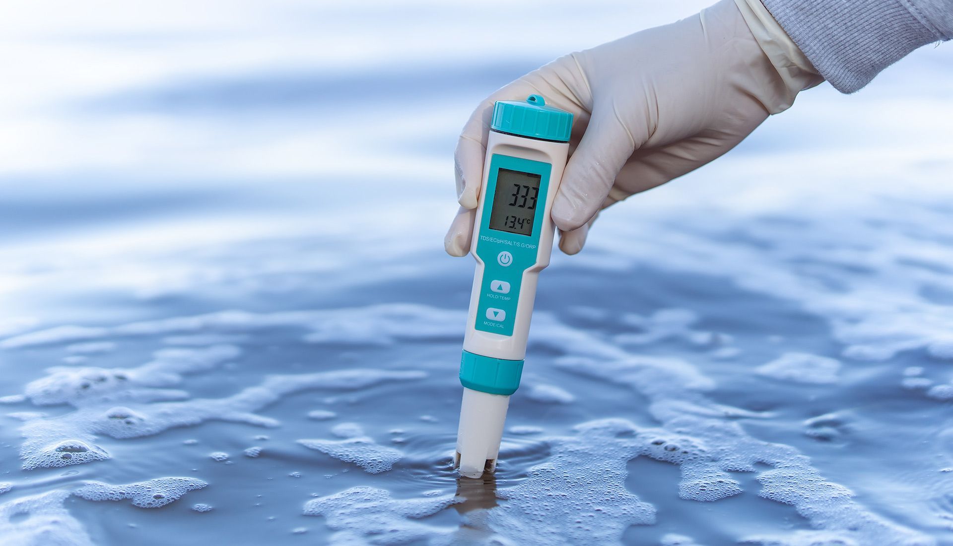 A person is holding a thermometer over a body of water.