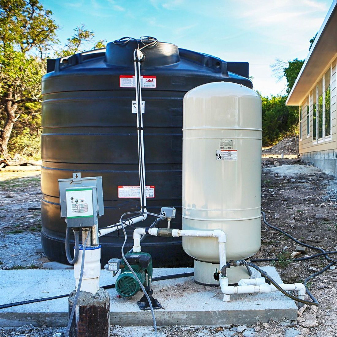 A black tank and a white tank are sitting next to each other in front of a house.