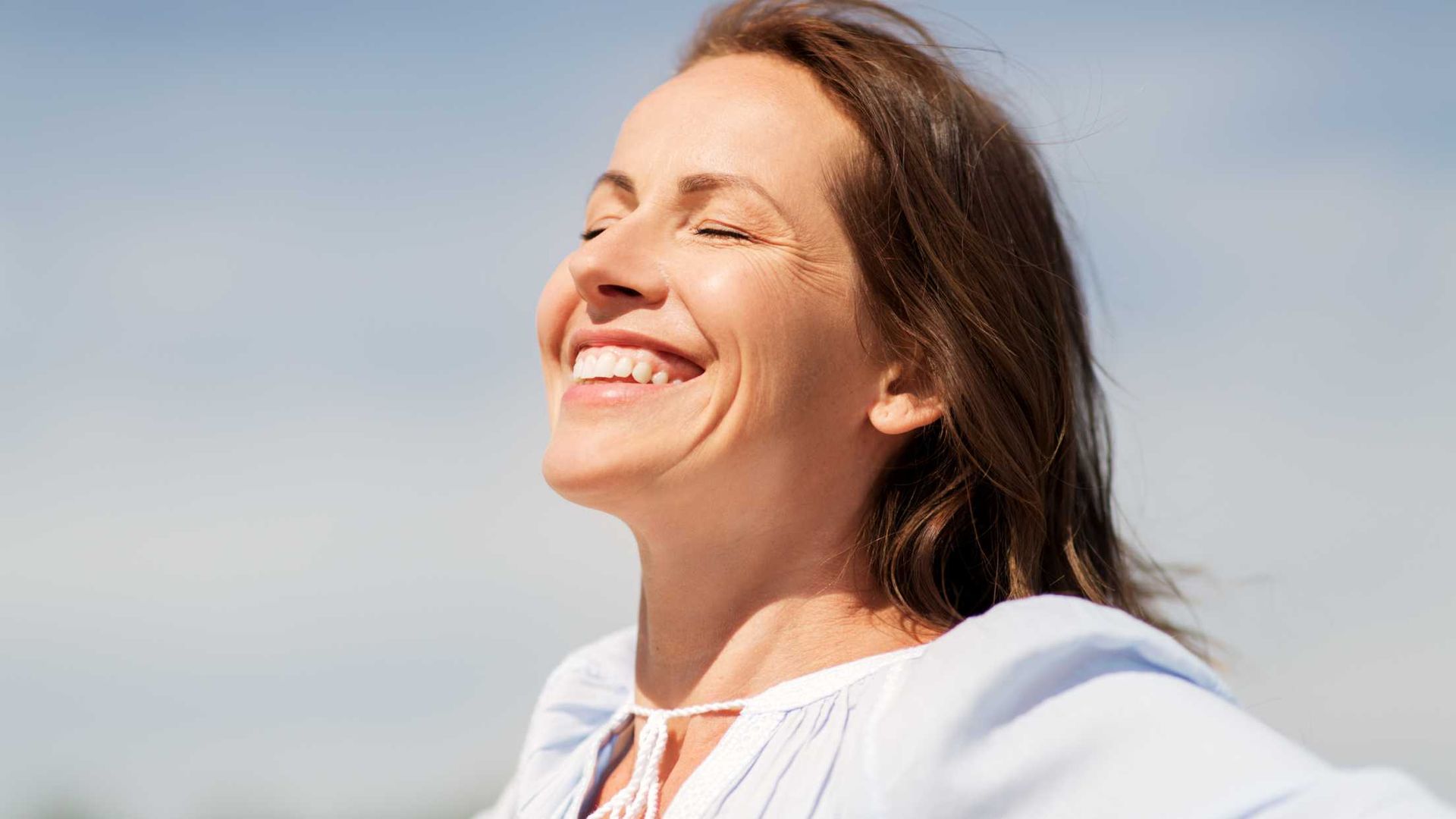 Woman smiling with eyes closed, enjoying the sun with blue sky background.