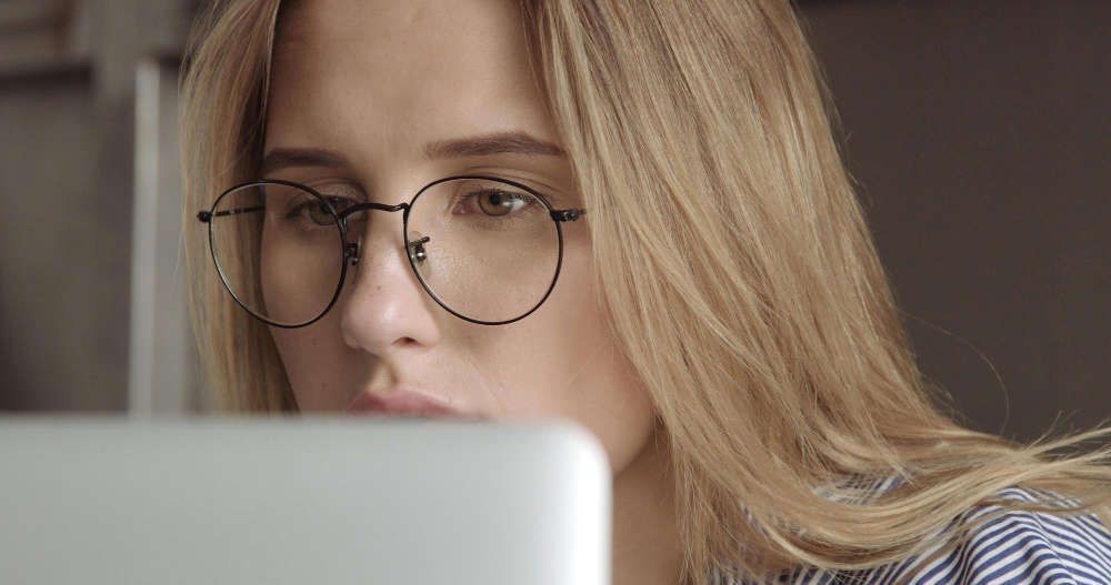a woman wearing glasses looks at a laptop.