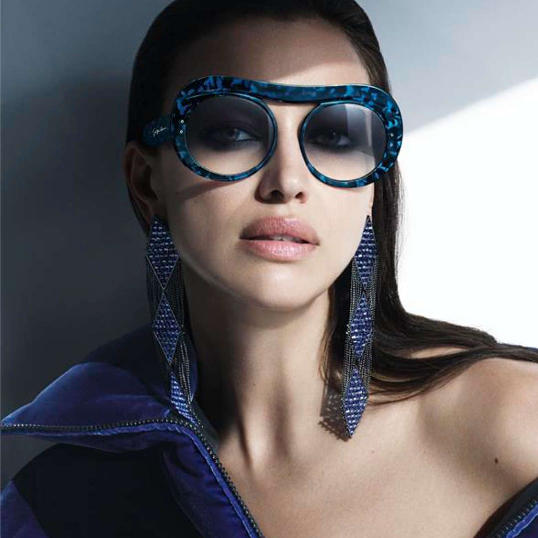 A woman wearing sunglasses and earrings is wearing a blue jacket