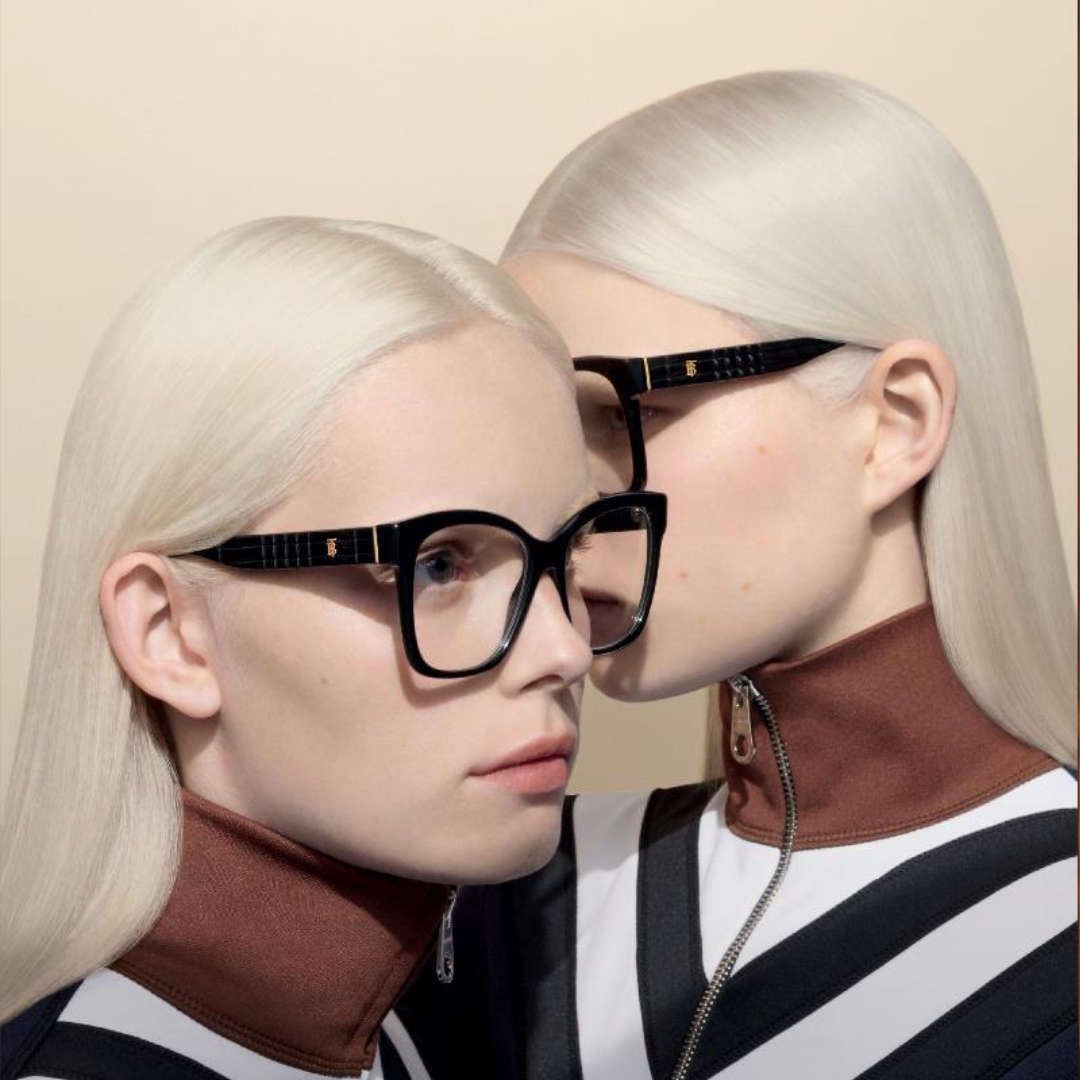 Two women wearing glasses are kissing each other on the cheek