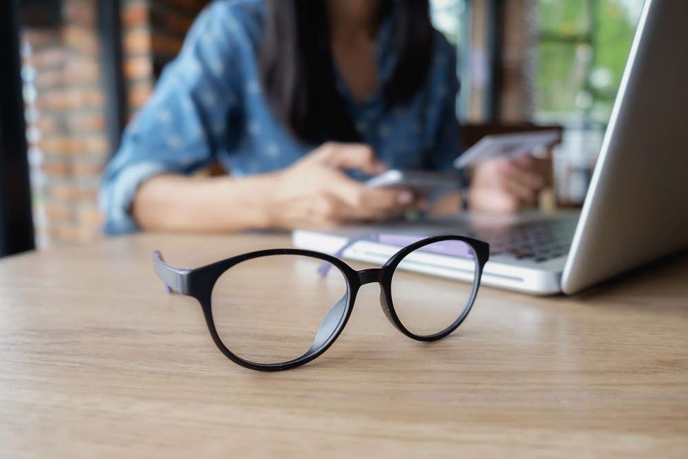 une paire de lunettes est posée sur une table en bois à côté d'un ordinateur portable.