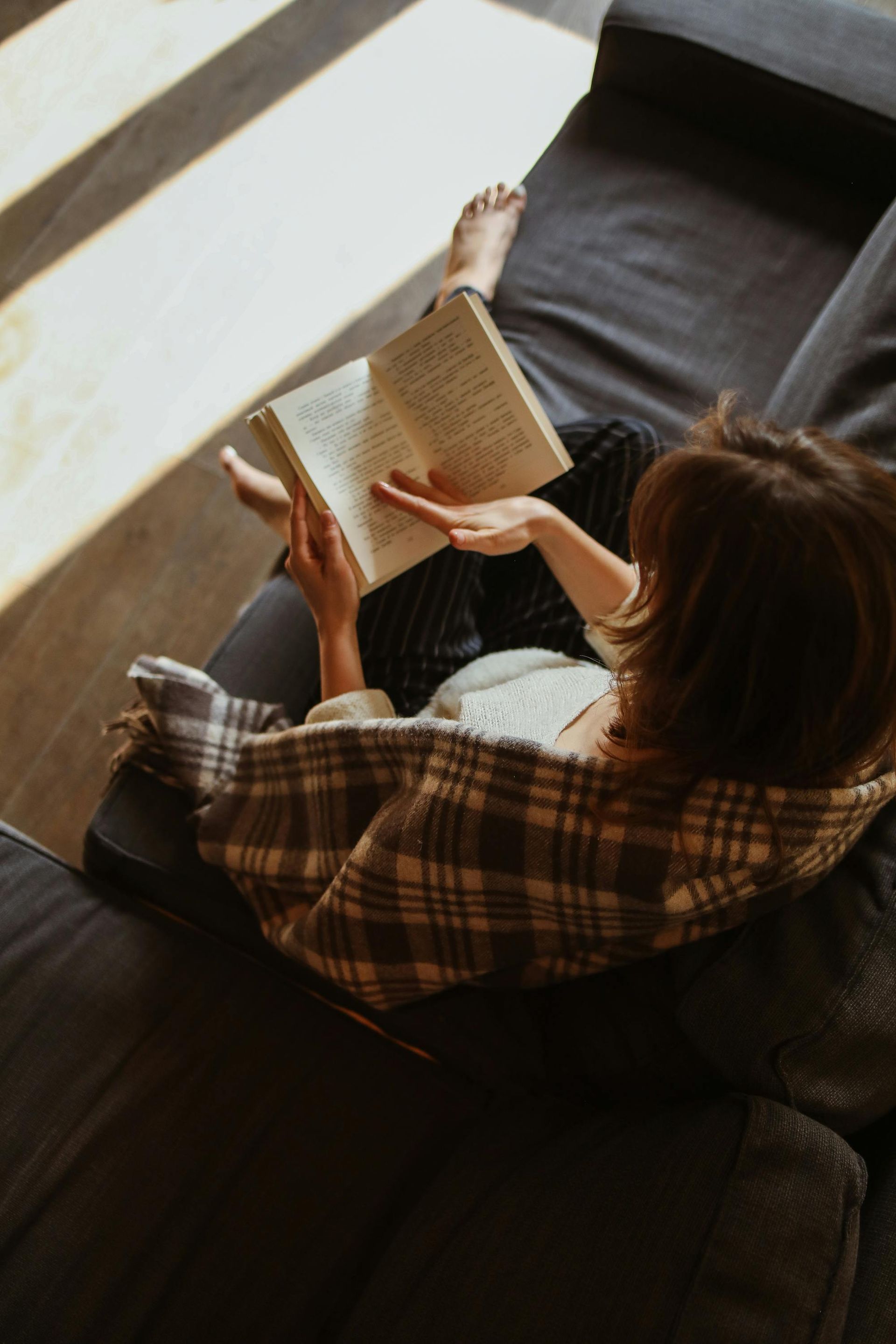 Une femme est assise sur un canapé et lit un livre.