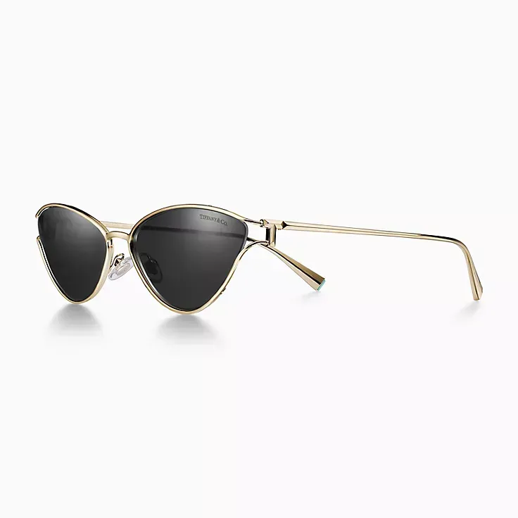 A pair of cat eye sunglasses with a gold frame and black lenses on a white background.