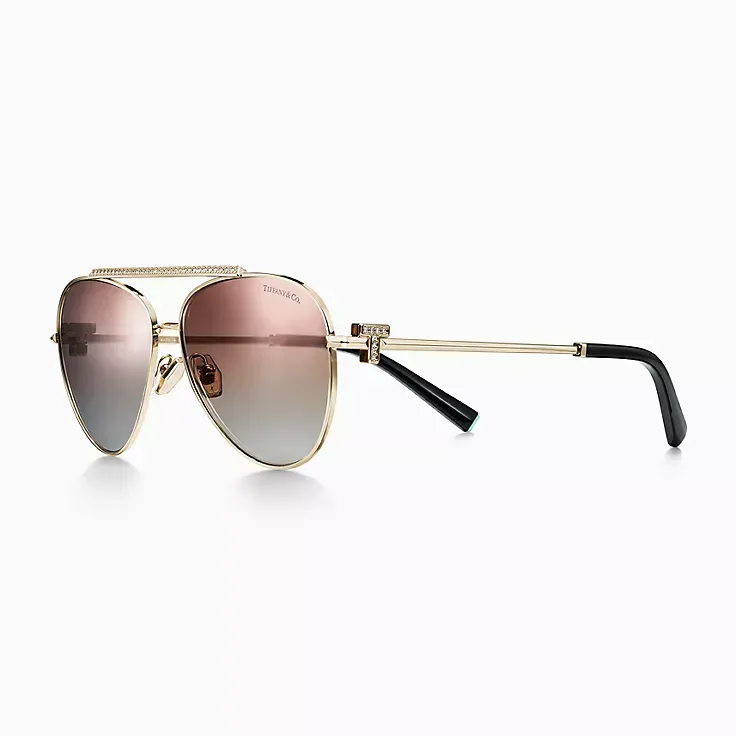 A pair of aviator sunglasses with a gold frame and pink lenses on a white background.