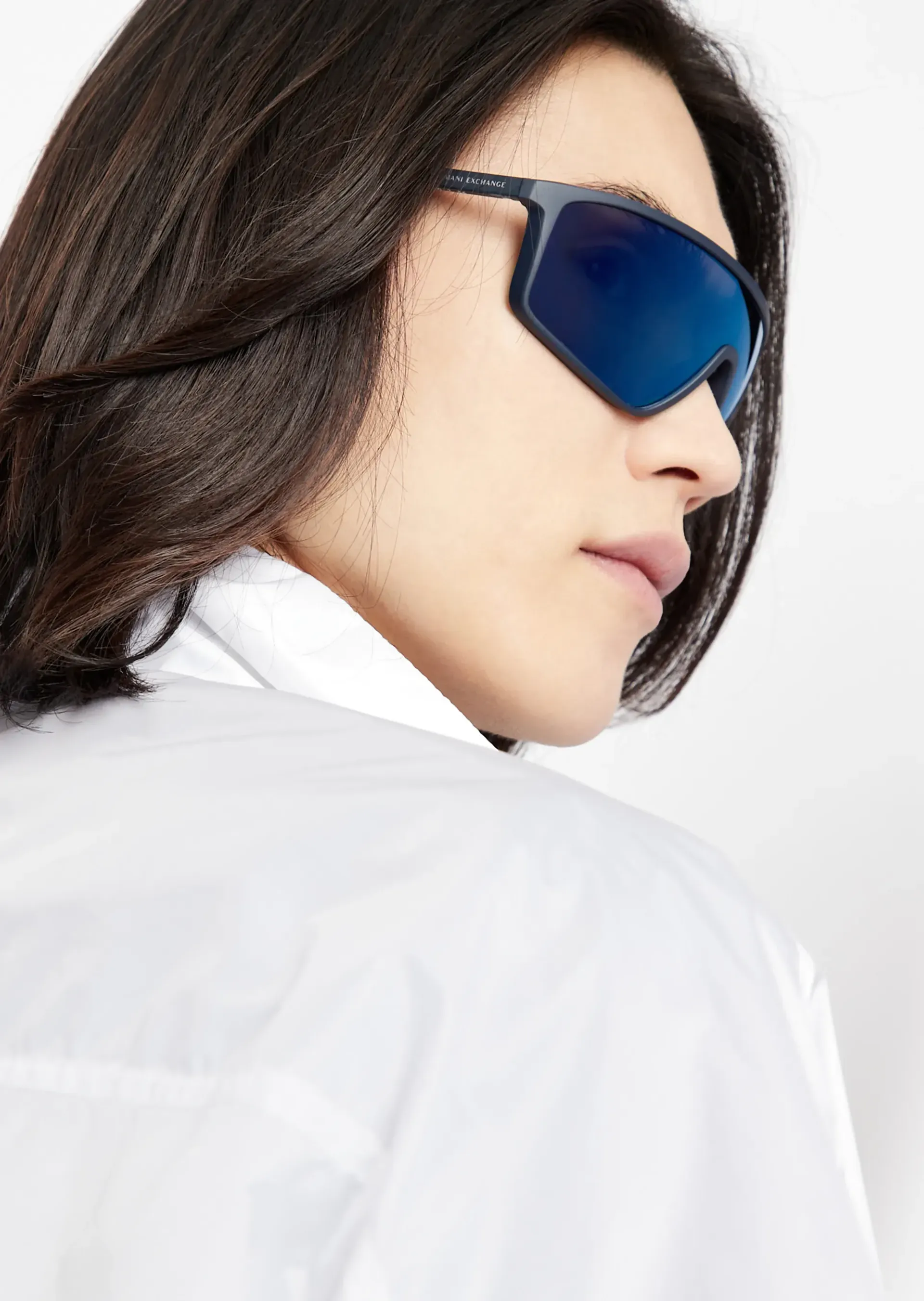 A woman wearing sunglasses and a white shirt is looking over her shoulder.