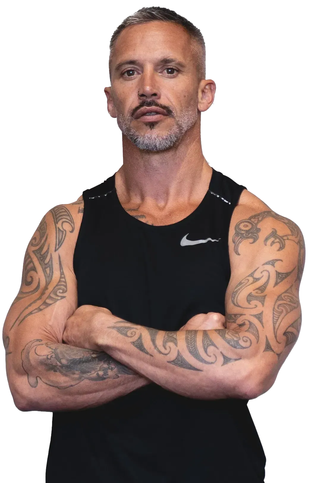 A man with tattoos on his arms and chest is standing with his arms crossed. TBW FITNESS 