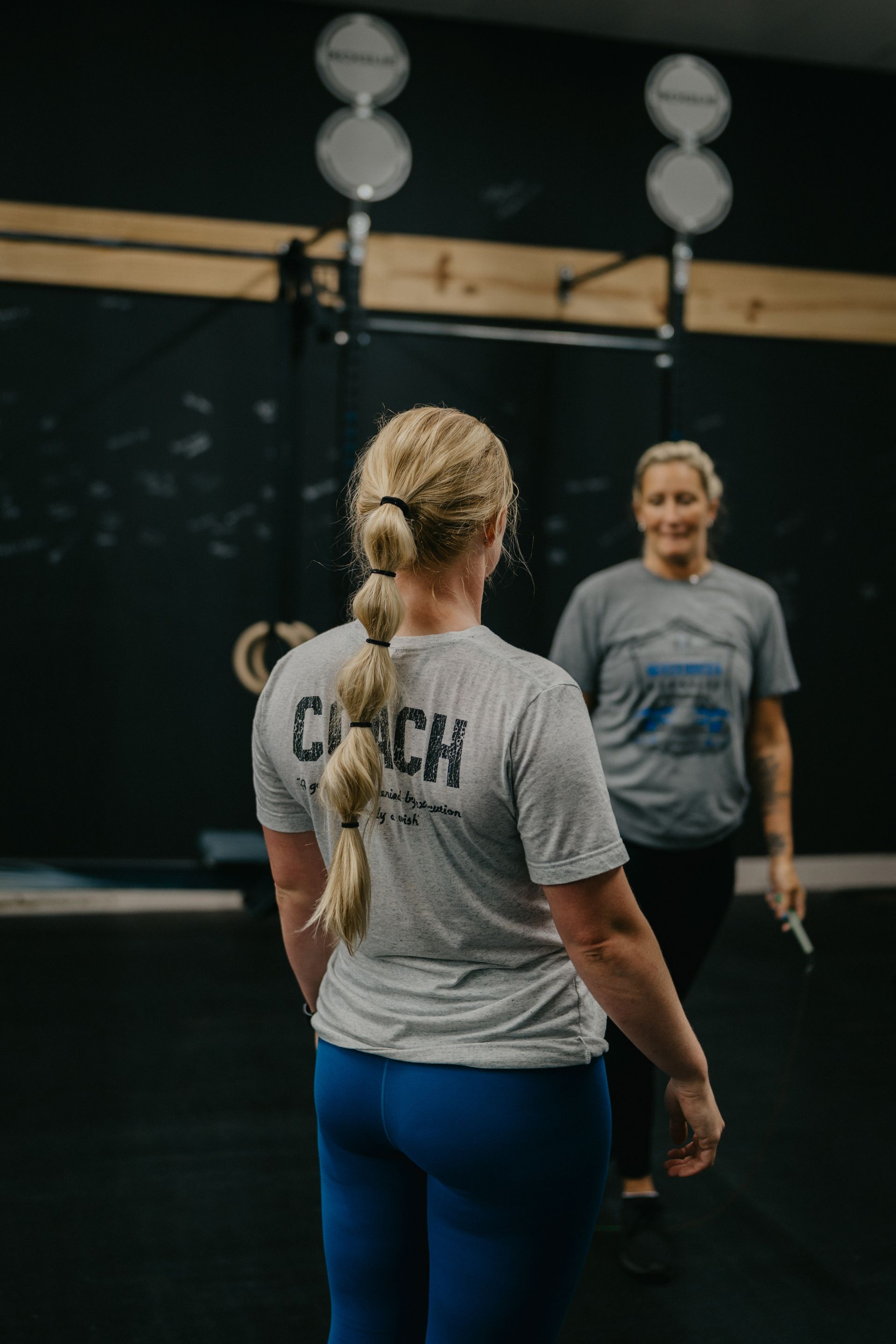A man is watching a woman do trx exercises in a gym.