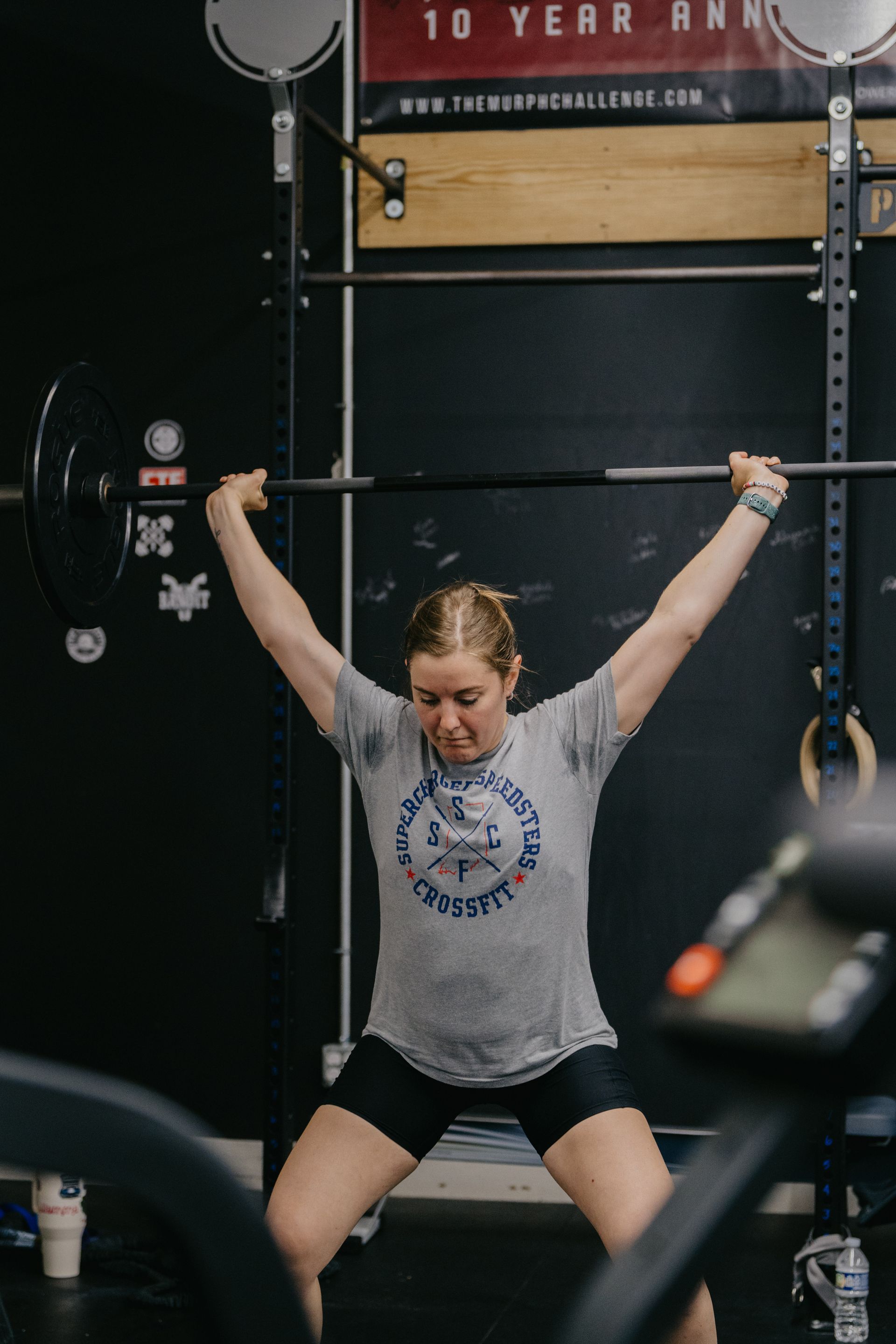 A man is lifting a barbell over his head in a gym.