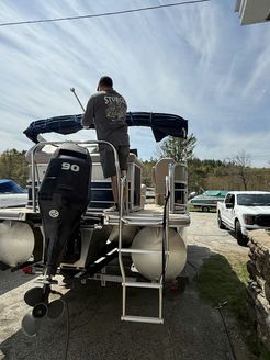 A man is standing on the back of a pontoon boat.