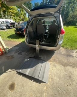 Silver minivan with an open ramp for wheelchair access. Outdoors, on concrete.