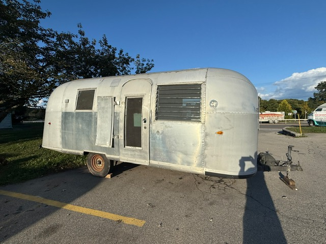 Vintage silver travel trailer parked on asphalt.