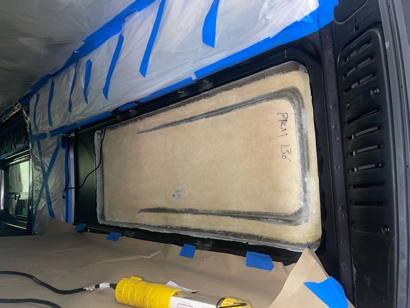Interior of a vehicle being worked on. Window frame with masking and a tool with a yellow handle.