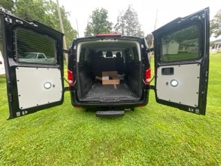 Back of a black van with doors open on a grassy lawn. Door interiors are gray and have circular lights.