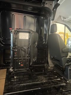 Inside a black van, showing a seat and large electronic equipment.