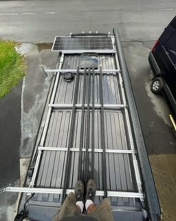 Person stands on a van roof with solar panels and metal support structures.