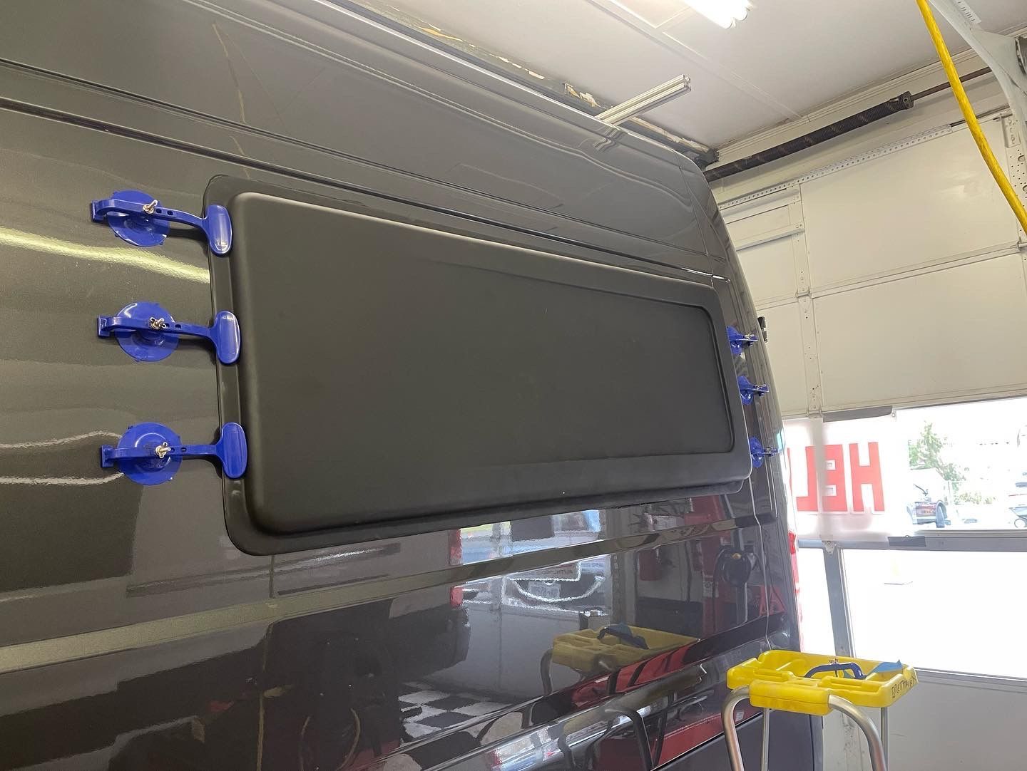 A dark grey van with a rectangular window, blue latches, and a bright red and white sign in the background.