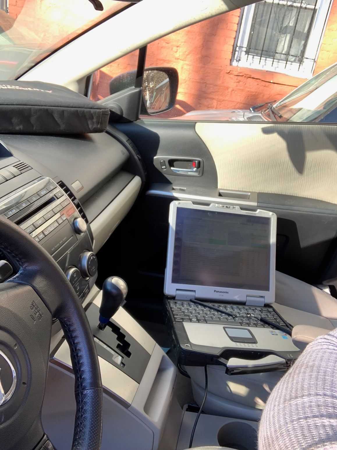 Inside car with laptop on passenger seat, person in the frame, steering wheel visible.