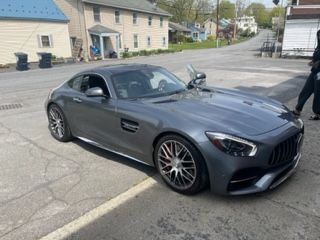 Gray Mercedes-AMG GT sports car parked on a street, with a person standing nearby.