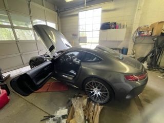 Gray sports car with hood and door open inside a garage.