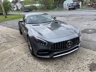Gray Mercedes-AMG GT sports car parked on a concrete surface, in front of a building.