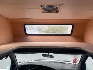 Interior view of a camper van showing bed over the cab, window, and dashboard.