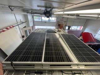 Three solar panels on a van roof inside a garage. White roof, black panels.