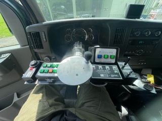 Interior view of a vehicle's dashboard, showing steering wheel and control panel with buttons, and display screens.