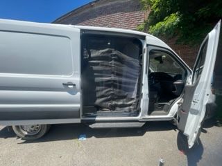 White cargo van with open side door and bags inside.