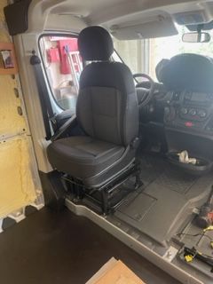 Interior of a van with a driver's seat installed. The seat is black, and the van's interior is under construction.