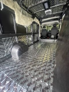 Interior of a van, insulated with silver sound-dampening material and insulation. The seats and front area are visible.