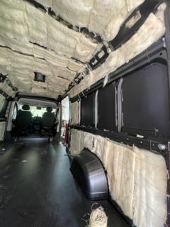 Interior of a van insulated with fluffy, light-colored material. Black flooring, windows, and seats are visible.