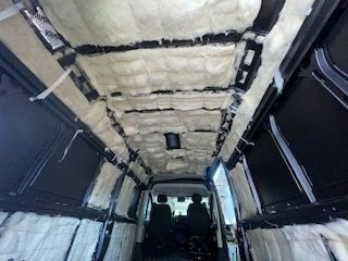 Van interior insulated with white insulation and black framing. Two people sit in front seats.