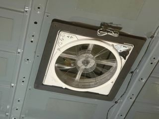 Ceiling fan in a van, gray with a black frame and open to the interior.