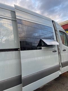 White van with tinted window partially open. Sunlight reflects off its surface.