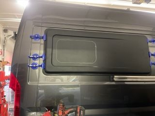 Black van with a window being installed, held in place with blue suction cups.