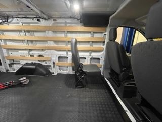 Interior of a van with wooden shelving along the side wall. A fold-down seat is positioned in the middle.