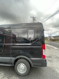Black van parked on the side of a road, cloudy sky above.