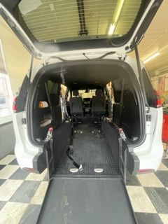 White van interior with ramp lowered, revealing accessible seating. Black flooring, checkerboard pattern below.