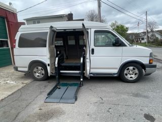White handicap-accessible van with open side door and lowered ramp on a street.