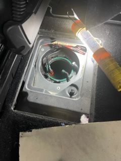 Open fuel tank access panel in car floor, illuminated by a flashlight.