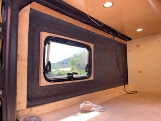 Interior view of a van conversion with a window, insulation, and wooden paneling.