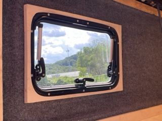 Window in wooden frame with a view of trees and sky.