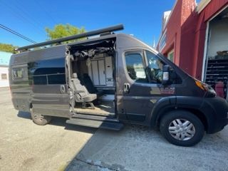 Grey camper van with open door, parked next to a building on a sunny day.