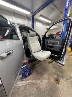 A silver truck with a disabled access seat extended. The door is open in a garage setting.